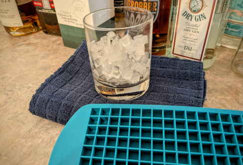 a rocks glass filled with many tiny ice cubes. In front is a tray that is very flat and looks as though it could fit roughly 80 of the small cubes