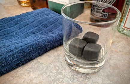a lone rocks glass containing three opaque, dark gray cubes, which are literal rocks