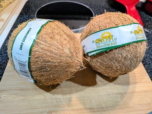 two coconuts on a cutting board, both still with a brand wrapper. The wrapper on one reads “DRY COCONUT”.