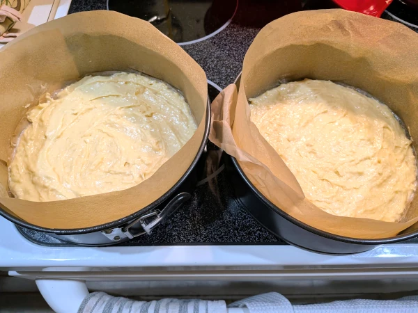 Two cake pans lined with parchment paper and filled with cake batter.
