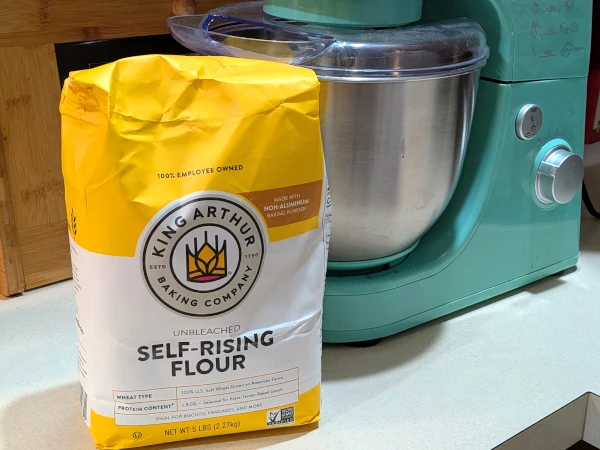 A yellow bag of King Arthur Baking Self-Rising Flour in front of a stand mixer.