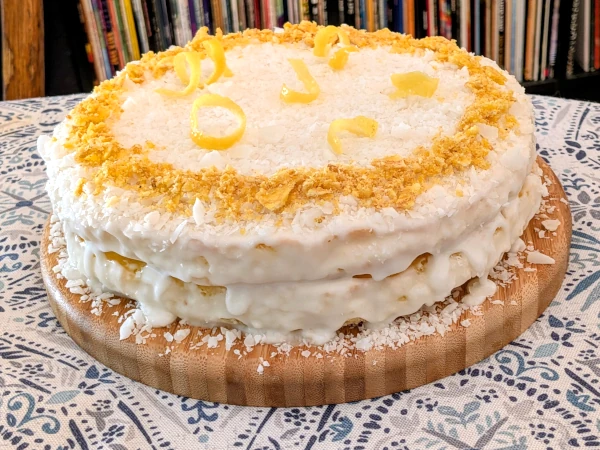 The finished cake: two layers with white, coconut-coated icing and topped with lemon peel swirls and a ring of crushed plantain chips.