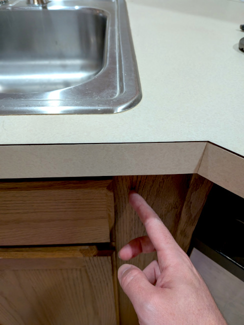 A photo of the countertop, with a finger pointing out the side of the cabinet. The edge of the sink extends just beyond this.
