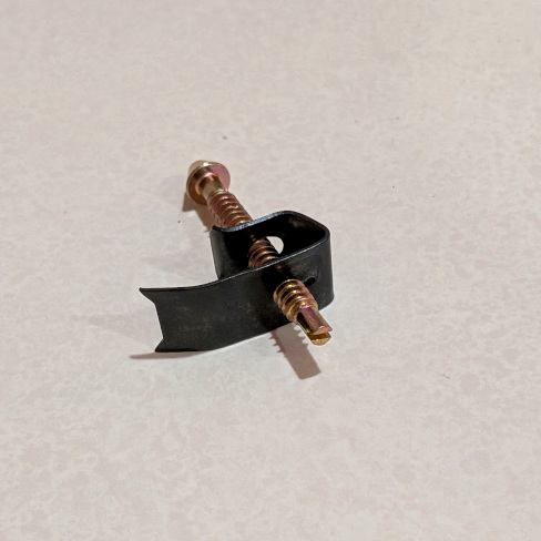 A photo of a clip and screw. The screw is flat on the bottom, where the slot to insert a flathead screwdriver resides. The screw has been inserted through both holes of the clip, which resembles a flat piece of metal bent into a J-shape. The corners of the longer end are pointed to dig into the underside of the countertop.