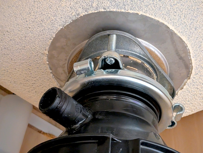 A photo of the top of the garbage disposal, taken in the cabinet below the sink. It shows both the screws and the metal loops.