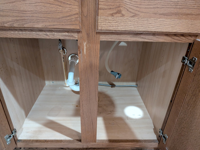 A photo of the cabinet under the sink with both doors open, showing it is largely empty.