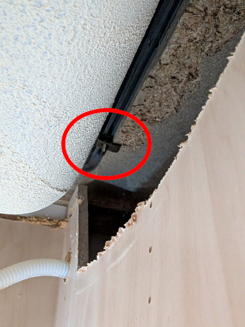 A photo from under the sink; the top of the cabinet wall has been roughly and unevenly cut out, allowing some visibility into the space beyond. A sink clip in this space has been circled in red.