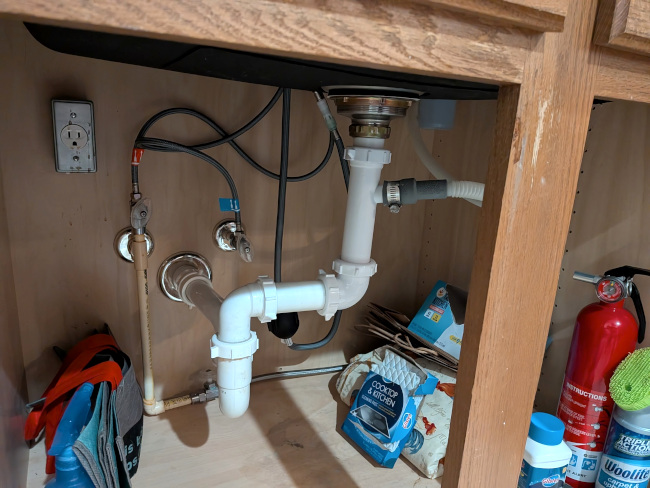 A photo underneath the kitchen sink, showing the completed pipework within the open cabinets. It ain't pretty, but it is functional.