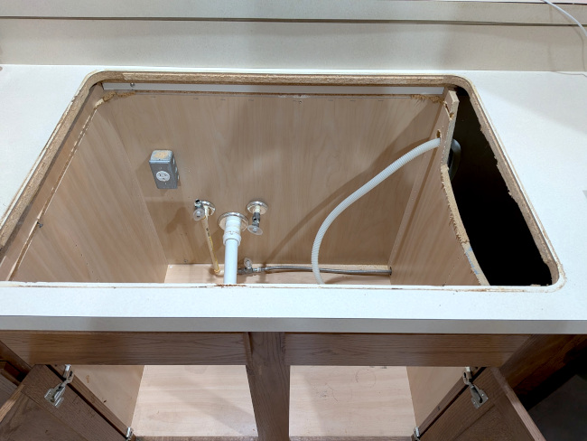 A photo showing the countertop where the sink used to be and the open cabinet space underneath.