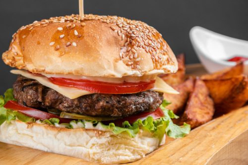 a photograph of a cheeseburge topped with veggies, with potato wedges in the background