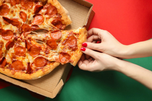 a photograph of two hands pulling a slice of pepperoni pizza out of a pizza box