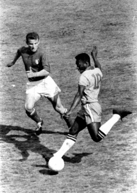 a black-and-white photograph of Pelé in-game, wearing jersey number 10, winding up to kick a soccer ball past a defender
